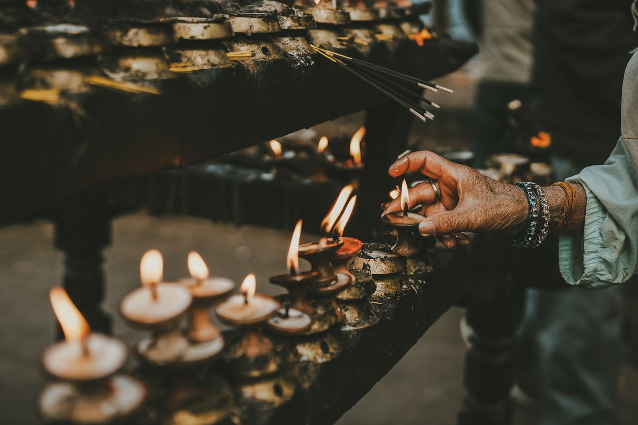 Hand lighting oil lamps during a traditional ritual with incense sticks, creating a spiritual and serene atmosphere.